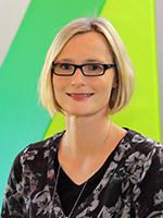 Portrait Andrea Kager, blonder Pagenkopf, Brillenträgerin, dunkles Shirt vor grünen Hintergrund